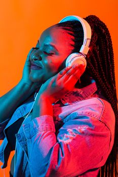 African american young woman listening to music online dancing and singing with headphones, neon light. Music and technology concept.