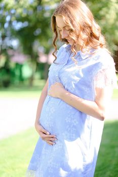 Happy pregnant woman wearing blue dress holding belly.