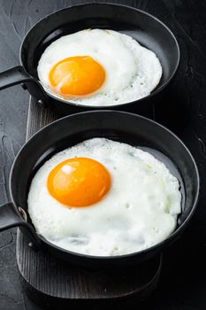 Fried eggs with bacon and vegetables in cast iron frying pan, on black background