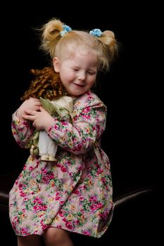 A little girl plays with a doll on a black background.
