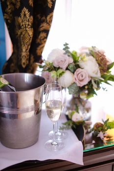 Bucket with champagne, wineglass and flowers on table.