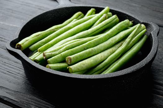 Fresh green French beans, in frying cast iron pan, on black wooden table background