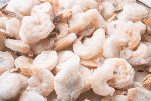 Pink frozen shrimps with ice. Uncooked peeled seafood, on plate, on white background