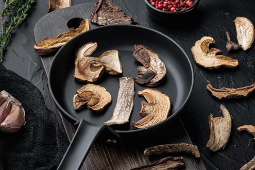Set of dried mushrooms in cast iron frying pan, on black background