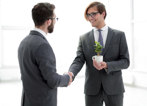 businessman with a sapling shaking hands with a partner.
