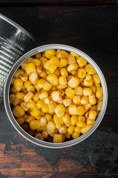 Lot of pieces of canned yellow corn in metall can, on old dark wooden table background, top view flat lay