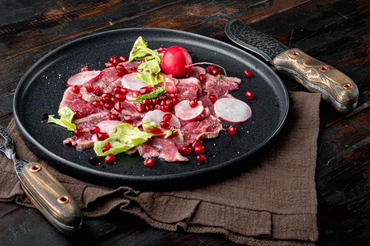 Beef Carpaccio cold appetizer, with Radish and garnet, on plate, on old dark wooden table background