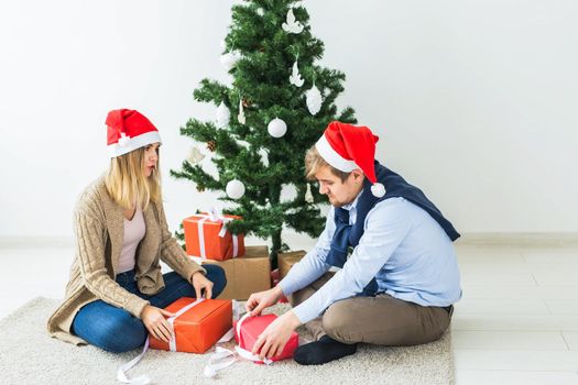 Christmas and holidays concept - Young happy couple wearing santa hats opening gifts at home.