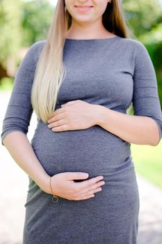 Young pregnant woman wearing grey dress holding belly.