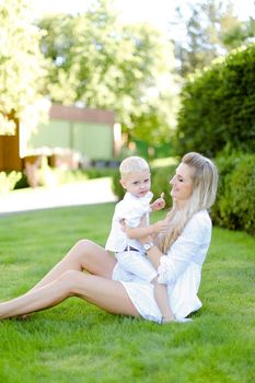 Young pretty mother sitting with little baby on grass in yard.