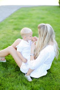 Young mom sitting with little baby on grass in yard.