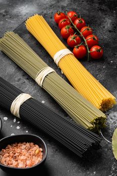 Multi colored spaghetti with ingredients, on black dark stone table background