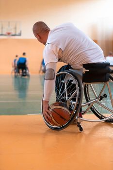 Disabled War veterans mixed race and age basketball teams in wheelchairs playing a training match in a sports gym hall. Handicapped people rehabilitation and inclusion concept