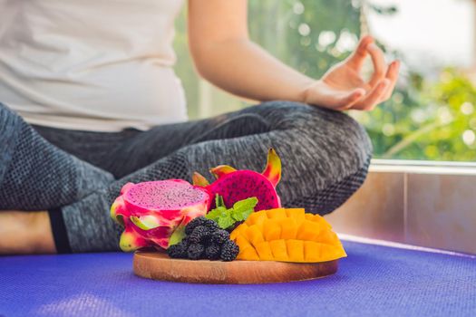hand of a woman meditating in a yoga pose, sitting in lotus with fruits in front of her dragon fruit, mango and mulberry