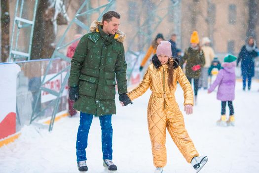 Young dad and adorable little girl have fun on skating rink outdoors