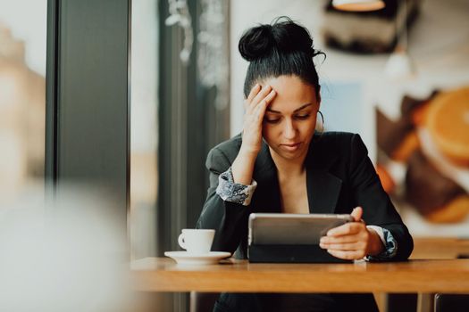 a Latina woman sits in a cafe and looks in disappointment at the tablet