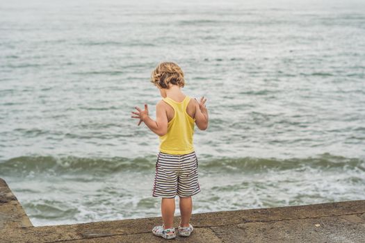 Cute boy stands on the shore watching the ocean waves