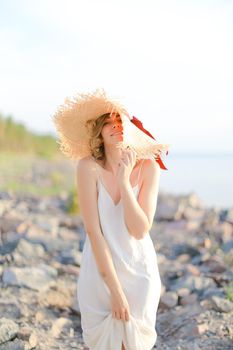 Young happy woman in hat standing on shingle beach.
