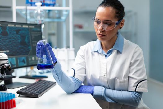 Biologist researcher holding transparent glassware analyzing blue solution