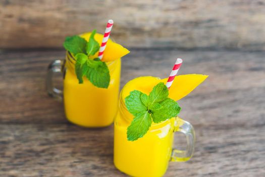 Juicy smoothie from mango in two glass mason jars with striped red straw on old wooden background. Healthy life concept, copy space