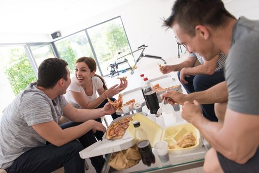 a group of young people cheerfully spending time while eating pizza in their luxury home villa
