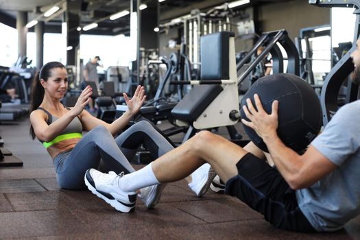 Fit and muscular couple exercising with medicine ball at gym.