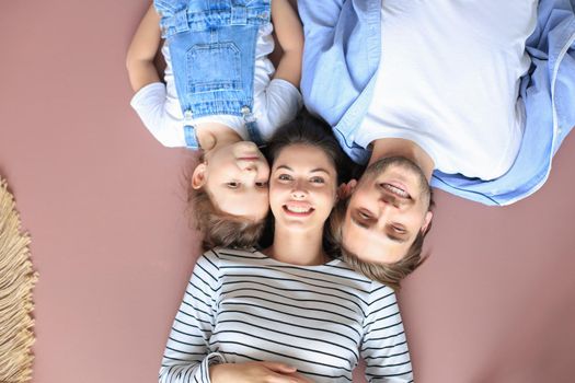 Top view portrait of smiling young parents with little preschooler daughter lying relaxing on warm floor at home, happy family with small child rest have fun at home.