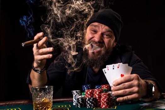 Bearded man drinking whisky and smoking a cigar while playing poker