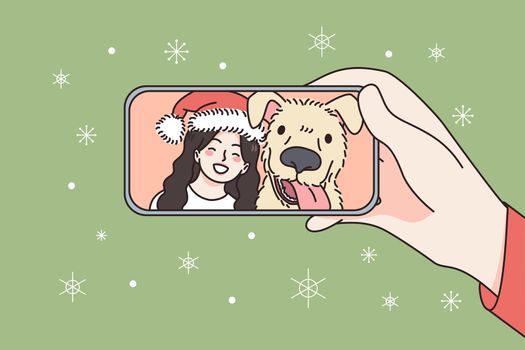 Online Christmas and New Year celebration concept. Human hand holding smartphone with smiling girl and dog in Santa hat celebrating and greeting online vector illustration