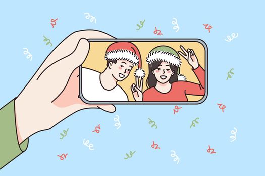 Online New Year celebration concept. Human hand holding smartphone with smiling couple in Santa hats celebrating and greeting online vector illustration