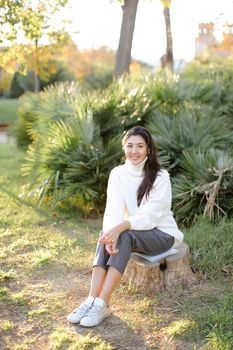 Korean girl sitting on stump in park.