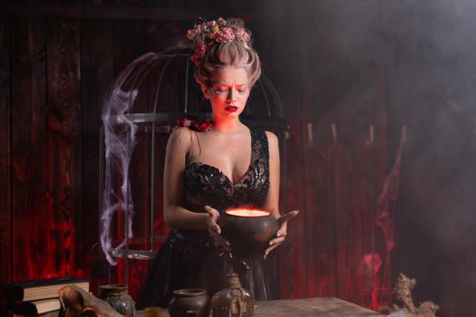 Halloween Witch with cauldron. Beautiful young woman conjuring, making witchcraft