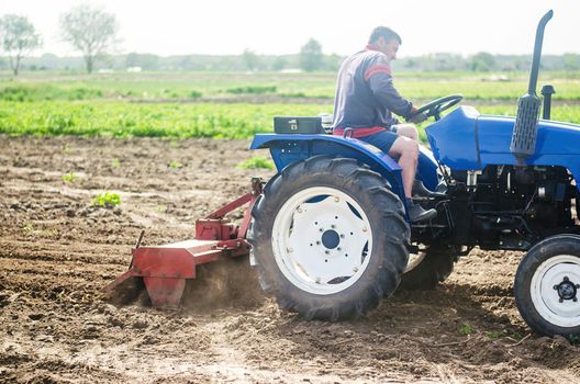 A farmer on a tractor cultivates a farm field. Soil milling, crumbling and mixing. Agriculture, growing organic food vegetables. Loosening the surface, cultivating the land for further planting.