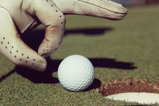 man's hand putting golf ball in hole