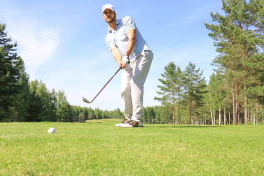 Full length of golf player playing golf on sunny day. Professional male golfer taking shot on golf course.