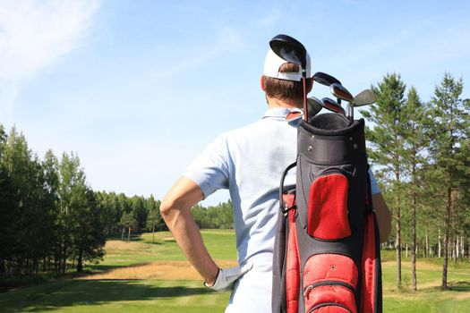 Golf player walking and carrying bag on course during summer game golfing.