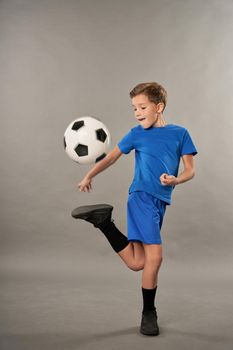 Little football player in sportswear kicking soccer ball