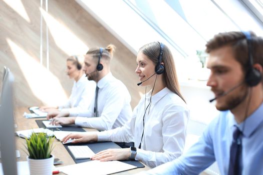 Female customer support operator with headset and smiling accompanied by her team.