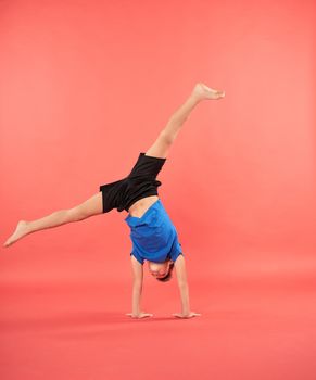 Sporty boy doing handstand exercise against red background