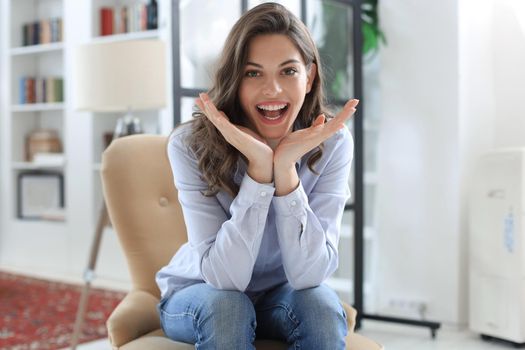 Woman happy on armchair smiling and stretching looking at camera.