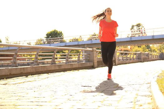 Beautiful young woman in sports clothing running while exercising outdoors.
