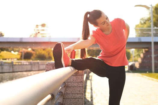 Attractive young fitness woman wearing sports clothing exercising outdoors, stretching exercises.