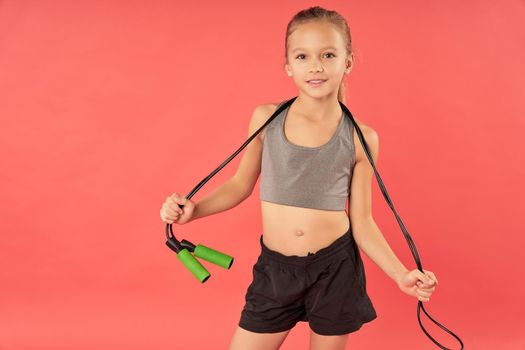 Cute girl with skipping rope standing against red background