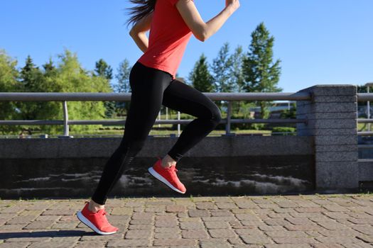 Modern young woman in sports clothing jumping while exercising outdoors.