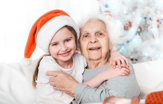 smiling granddaughter in santa hat hugging with grandma