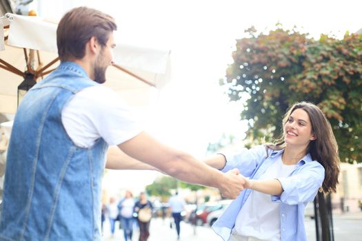 Beautiful young couple holding hands and spinning while standing on the city street.