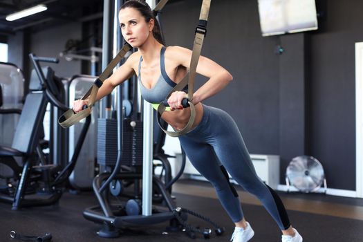 Muscular woman doing push ups training arms with trx fitness straps in the gym.