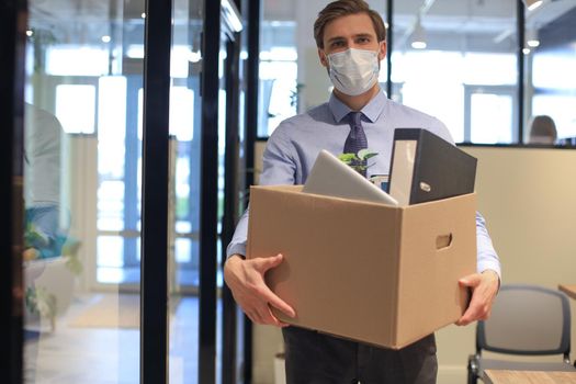 Dismissal employee in preventive medical mask in an epidemic coronavirus. Dismissed worker going from the office with his office supplies.