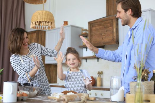 Cute little girl and her parents are having fun while cooking in kitchen at home together.
