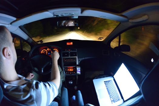 man working on laptop while drivig car on night